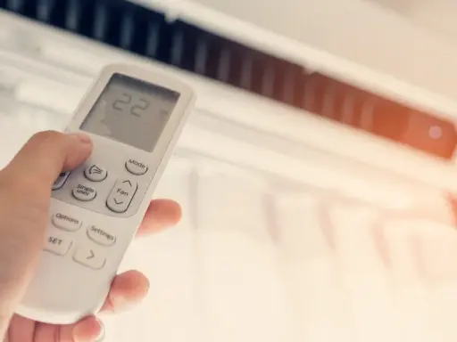 Mano ajustando el control remoto de un aire acondicionado, buscando la temperatura ideal en frigorías por m2 para un confort óptimo.