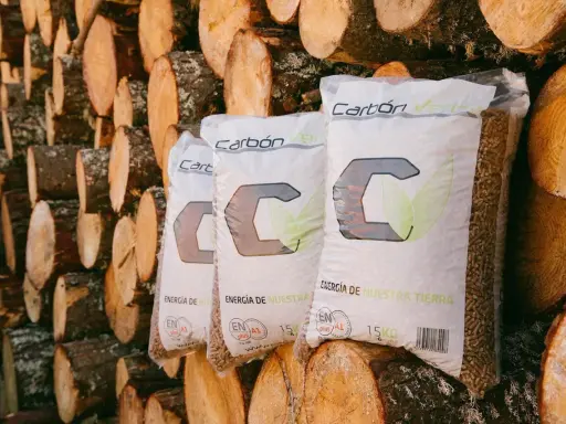 Bolsas de pellets de madera "Carbón Verde" apiladas contra troncos. Si tu estufa de pellets muestra un error 3, revisa la carga de combustible.