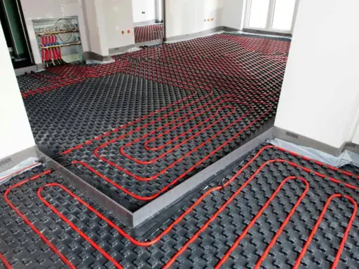 Instalación de suelo radiante aerotermia con tuberías rojas sobre paneles negros en una habitación en construcción.