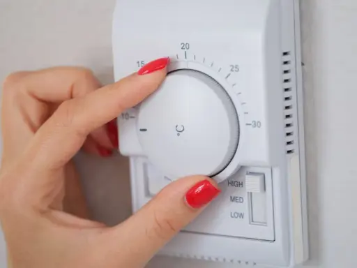 Mano ajustando el termostato para el cálculo de calefacción de la vivienda. La temperatura se muestra en grados Celsius.