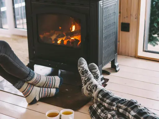 Pies con calcetines calentándose junto a una estufa de leña, disfrutando de la calefacción sin electricidad y una taza de té.