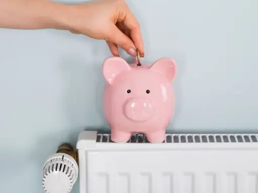 Mano inserta moneda en hucha rosa sobre radiador blanco. Ahorrando energía cuando se apaga la calefacción central.