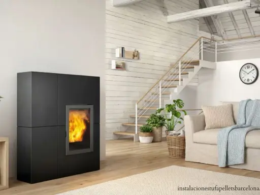 Estufa de pellets negra con fuego encendido, junto a escaleras y sofá. Ideal para un esquema de instalación de hidroestufas de pellets.