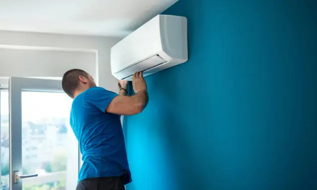 Técnico con carnet instalador aire acondicionado ajusta unidad interior en pared azul.