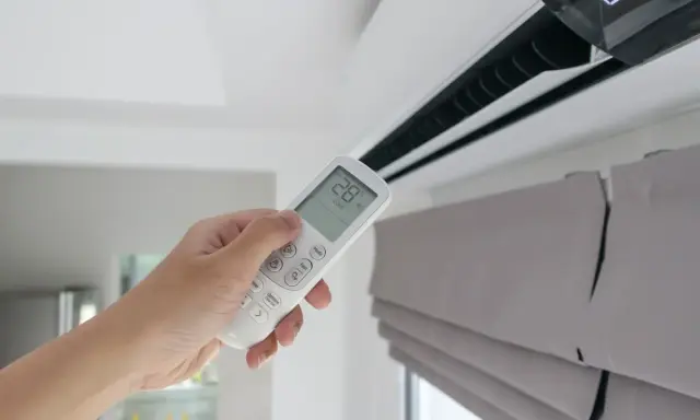 Mano sujetando control remoto de aire acondicionado, mostrando la diferencia entre climatizador y aire acondicionado.