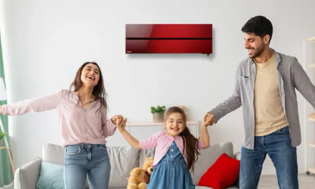 Familia feliz bailando bajo un aire acondicionado inverter rojo, disfrutando del confort y bajo consumo kwh.