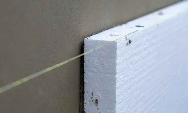 Instalación de aislamiento térmico para aislar tubos de calefacción exterior. Una línea guía de color amarillo ayuda a colocar el poliestireno.