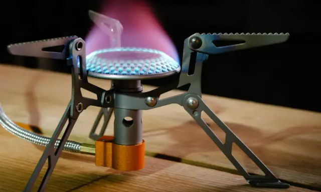 Estufa portátil sin electricidad ni gas, con llama azul y púrpura, ideal para acampar.
