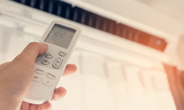 Mano ajustando el control remoto de un aire acondicionado, buscando la temperatura ideal en frigorías por m2 para un confort óptimo.