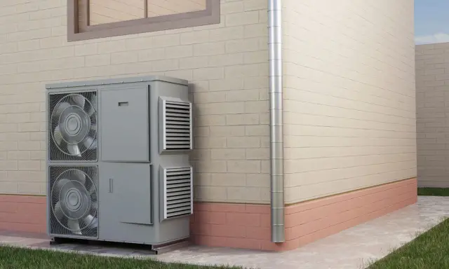 Unidad exterior de aire acondicionado para calefacción por inercia, instalada junto a una pared de ladrillo.