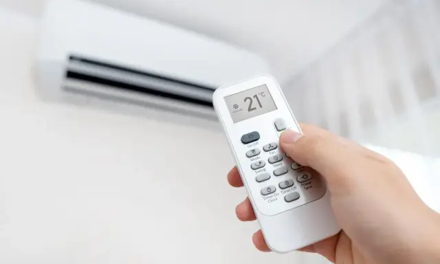 Mano ajustando el control remoto del aire acondicionado a 21°C, modo "Cooling". ¡Así se logra un ambiente fresco y agradable!