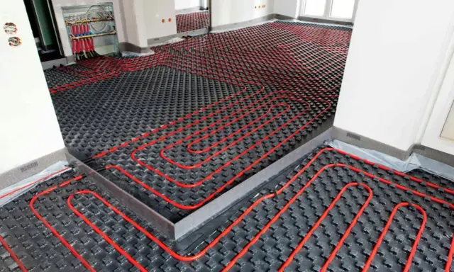 Instalación de suelo radiante aerotermia con tuberías rojas sobre paneles negros en una habitación en construcción.