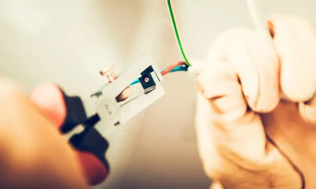 Manos con guantes pelando cables para como cambiar el termostato de la calefacción.