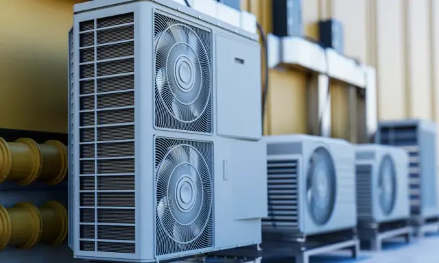 Unidades exteriores de aerotermia R290, con ventiladores y rejillas, alineadas junto a una pared amarilla y tuberías.