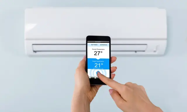 Mano ajustando la temperatura del aire acondicionado desde el móvil, facilitando conectar aire acondicionado a wifi para control remoto.