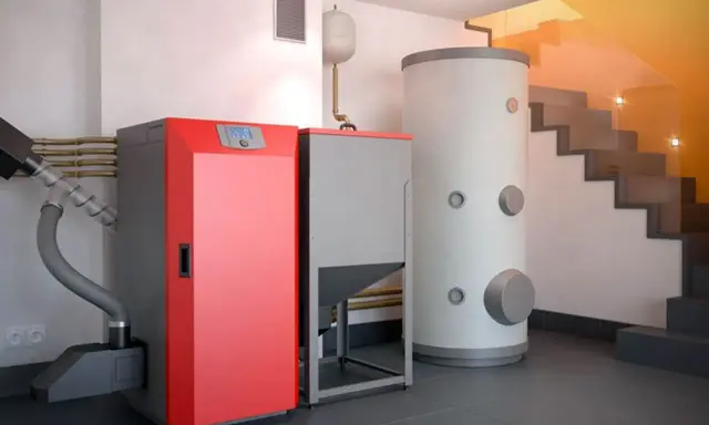 Moderna caldera de pellets roja y gris junto a un gran acumulador de agua. Una solución eficiente para cambiar caldera de gas por pellets.