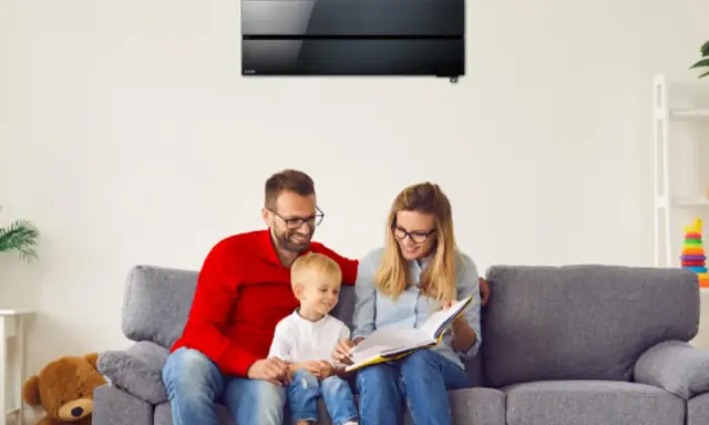 Familia feliz en el sofá, disfrutando de un momento tranquilo bajo el aire acondicionado de bajo consumo.