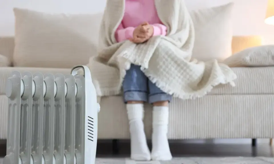 Radiador eléctrico junto a un sofá donde una persona se abriga. Una solución eficaz para los sistemas de calefacción del hogar.