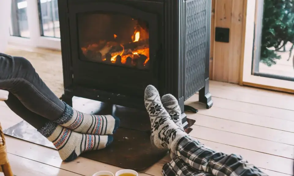 Pies con calcetines calentándose junto a una estufa de leña, disfrutando de la calefacción sin electricidad y una taza de té.