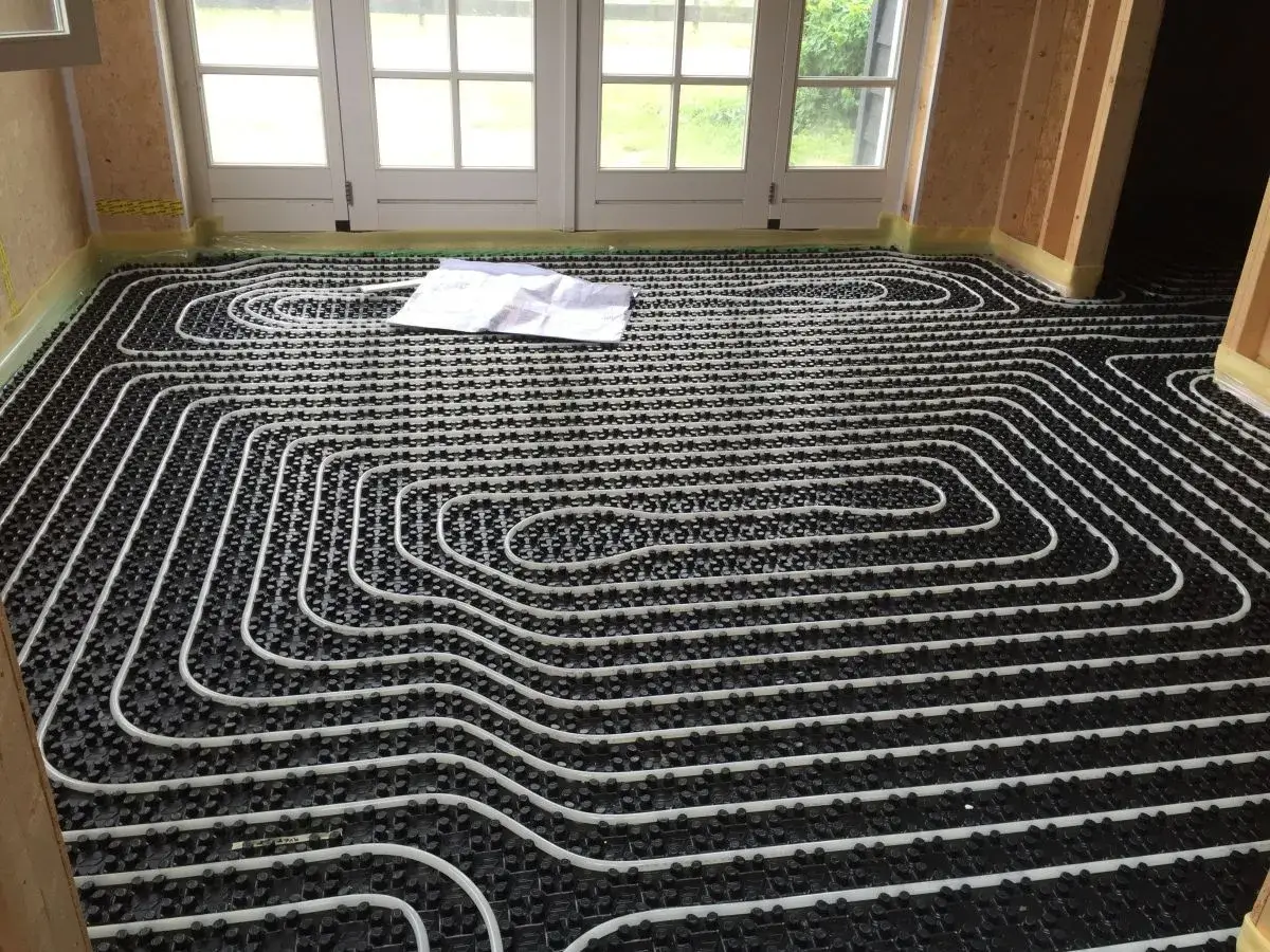 Instalación de tuberías blancas sobre paneles negros para un futuro suelo radiante. Un plano yace sobre el suelo.