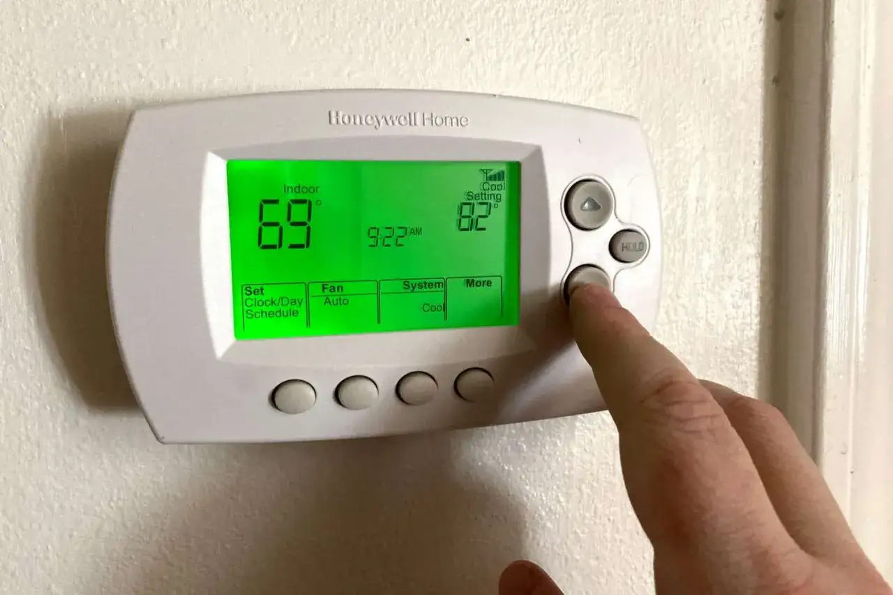 Dedo presionando bot&oacute;n para programar termostato digital Honeywell. Muestra 69&deg; interior y 82&deg; ajuste de enfriamiento.