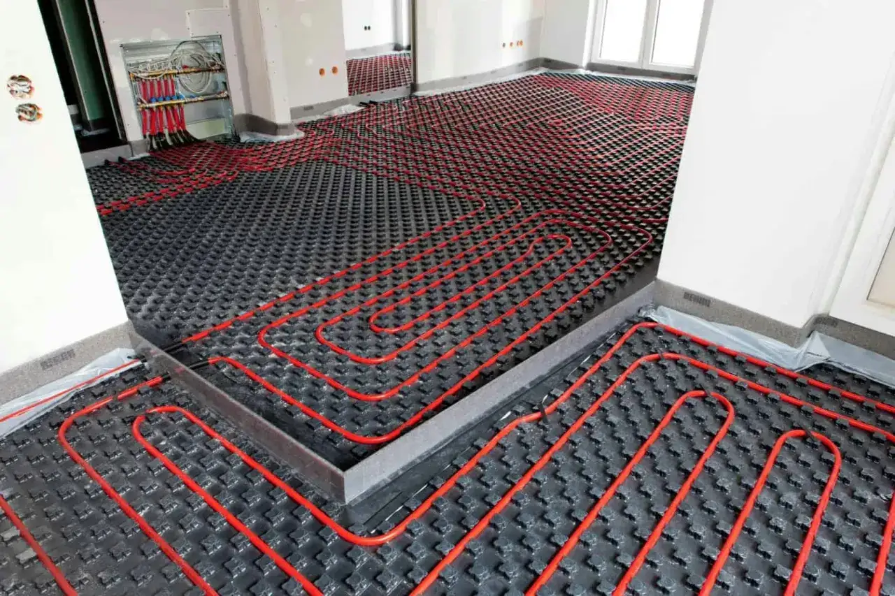 Instalaci&oacute;n de suelo radiante, una alternativa al gas en un piso, con tuber&iacute;as rojas sobre paneles negros.