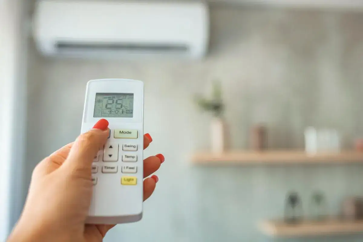 Mano con control remoto ajustando el aire acondicionado para un ambiente fresco y seco, como un deshumidificador.