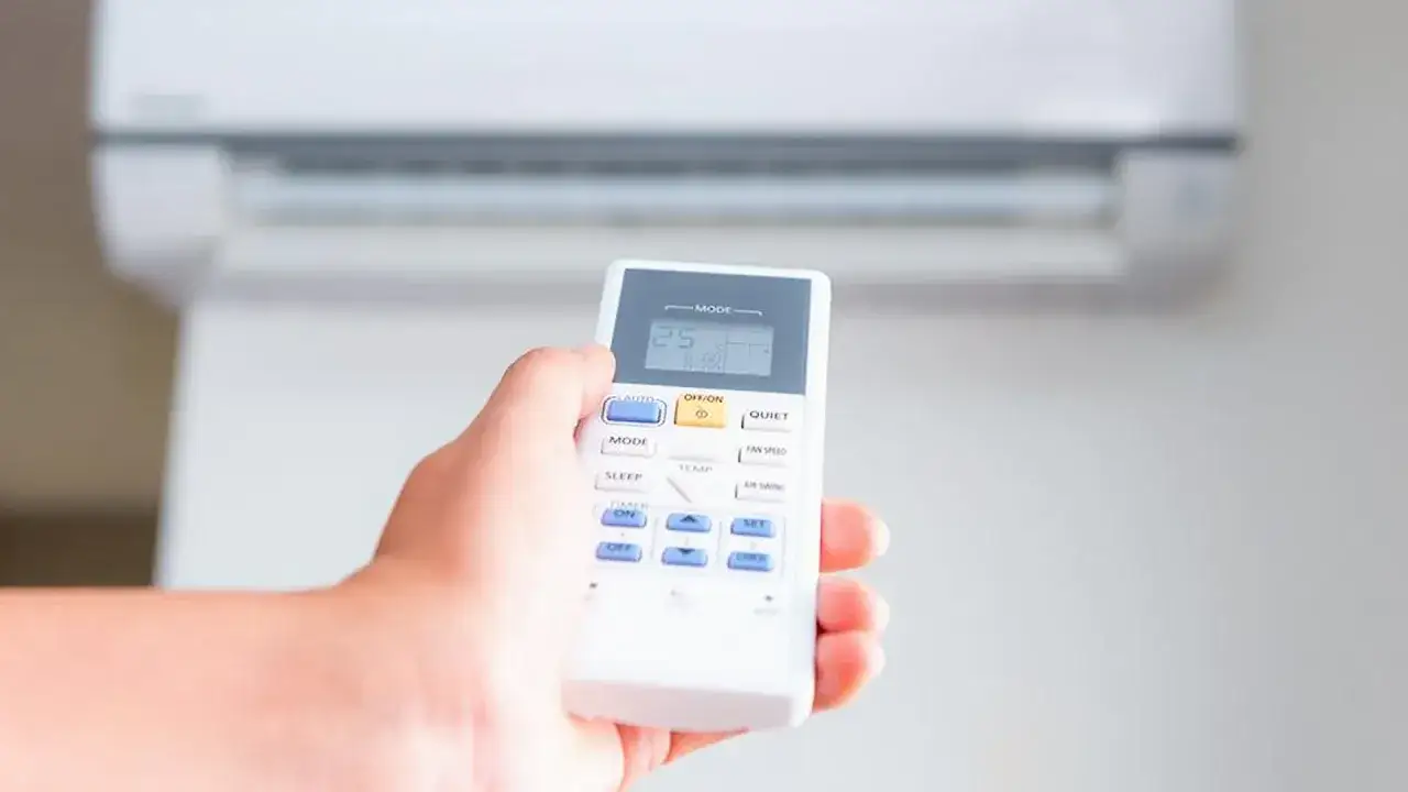 Mano sujetando control remoto para activar la bomba de calor del aire acondicionado. Muestra la temperatura a 25 grados.