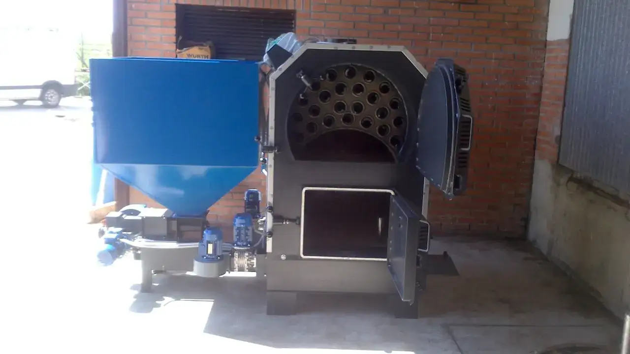 Caldera industrial con tolva azul, lista para quemar hueso de aceituna y generar energía.