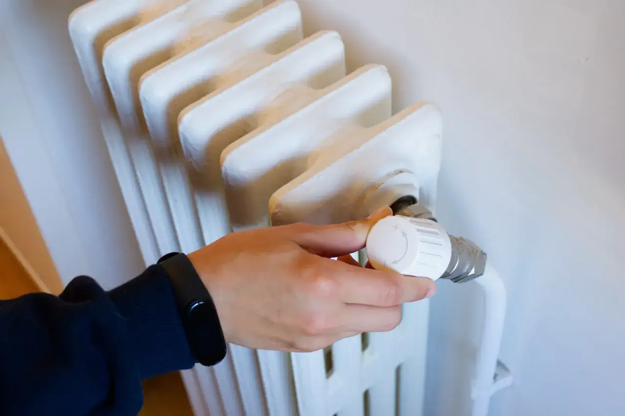 Mano ajustando el termostato de un radiador blanco para controlar la calefacción individual.