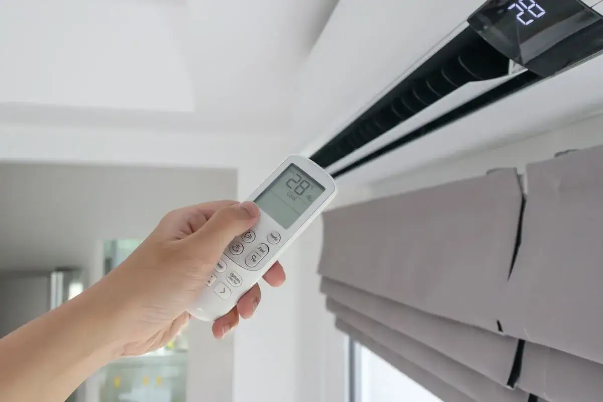 Mano con control remoto ajustando el aire acondicionado. Entender la diferencia entre climatizador y aire acondicionado es clave para tu confort.