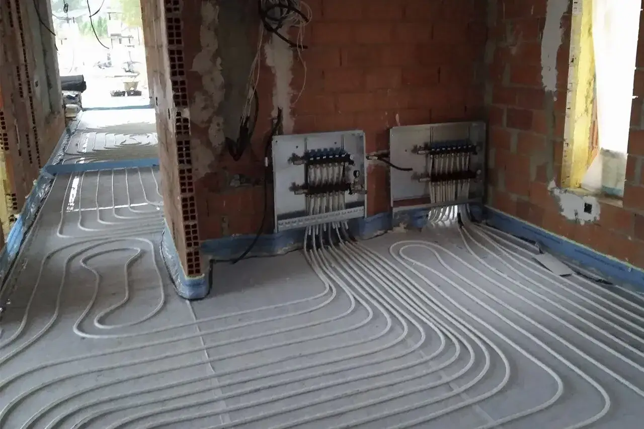 Instalación de tuberías para suelo radiante en una obra. Se ven colectores y tubos blancos serpenteando por el suelo.