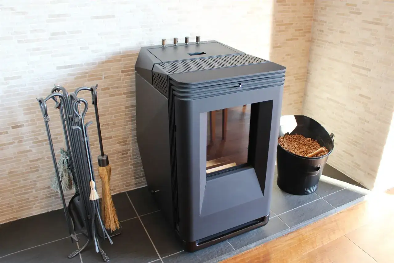 Estufa de pellets negra junto a un cubo de pellets y herramientas de chimenea. &iquest;Ser&aacute; el error 12 estufa pellets?