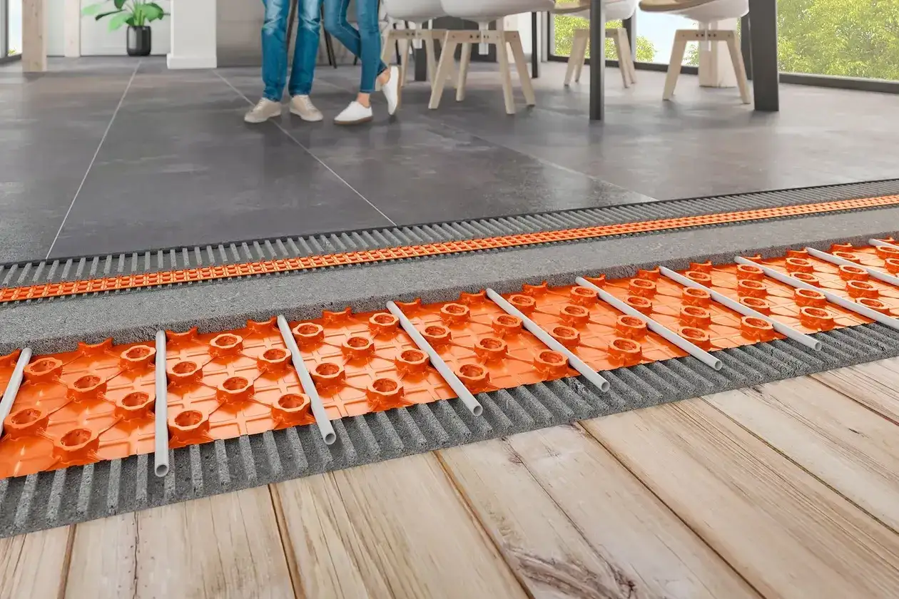 Sistema de calefacción antigua con tuberías naranjas bajo un suelo de baldosas y madera.