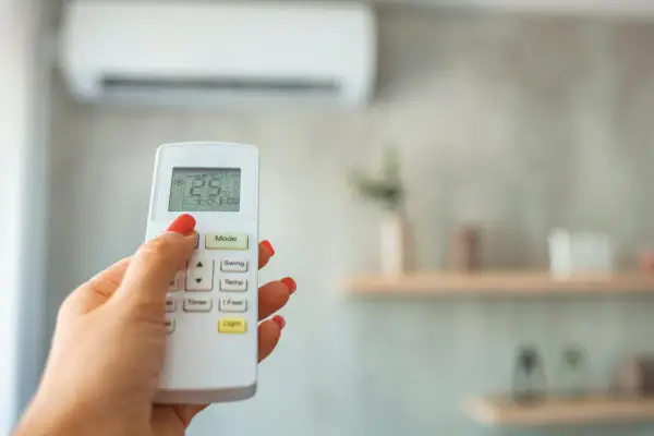 Mano con control remoto ajustando el aire acondicionado, buscando la temperatura ideal.