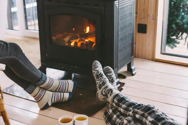 Pies con calcetines calentándose junto a una estufa de leña, disfrutando de la calefacción sin electricidad y una taza de té.