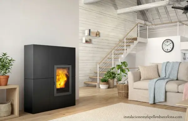 Estufa de pellets negra con fuego encendido, junto a escaleras y sofá. Ideal para un esquema de instalación de hidroestufas de pellets.