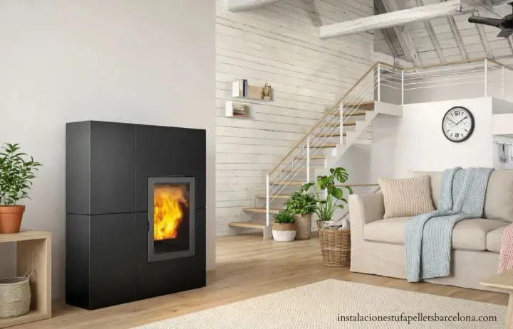 Estufa de pellets negra con fuego encendido, junto a escaleras y sofá. Ideal para un esquema de instalación de hidroestufas de pellets.